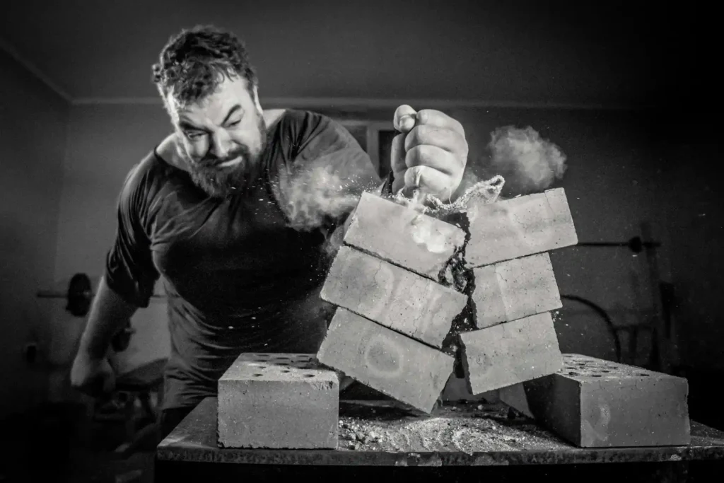 Brutal strong athlete smashing brick with fist – representing peak male energy, power, and natural testosterone boosters